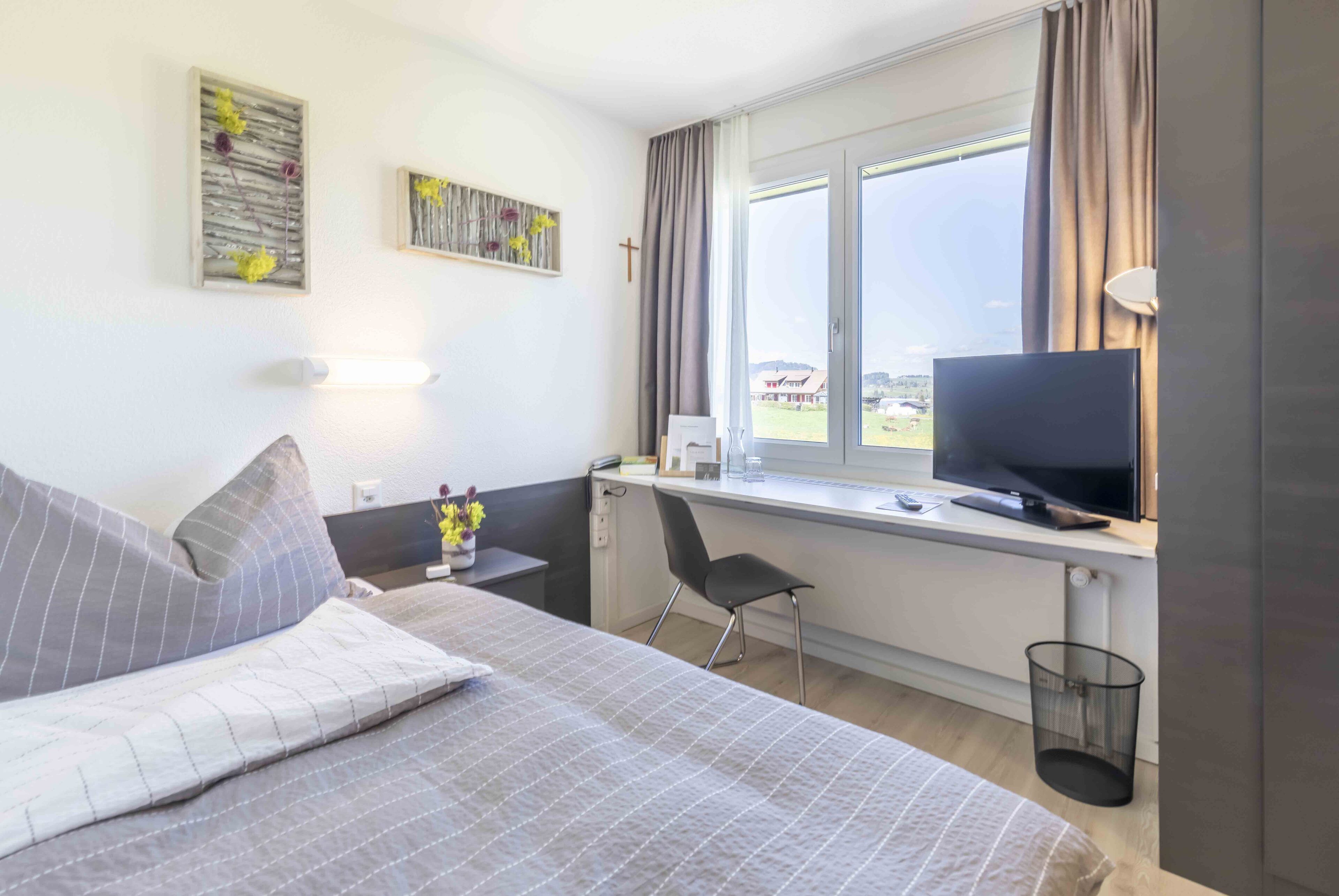 Een hotelkamer met een bed, een bureau met een televisie, een stoel en een raam met gordijnen.
