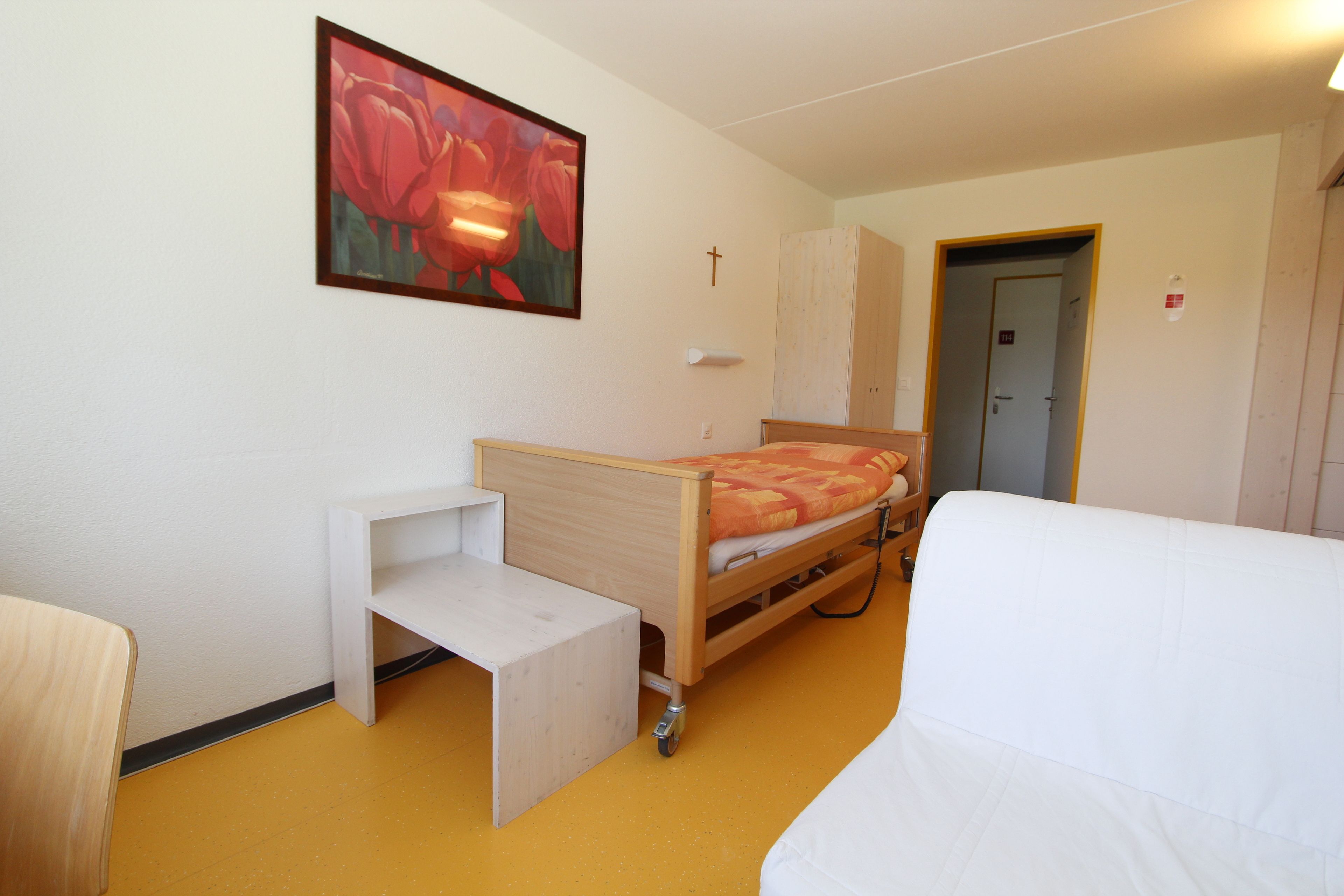 A bedroom with a bed, a bedside table, a chair, a wooden cabinet, and a painting on the wall.