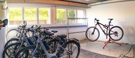 Zona de guardado para bicicletas con varias unidades, un soporte rojo para bicicletas y vistas a la vegetación exterior.
