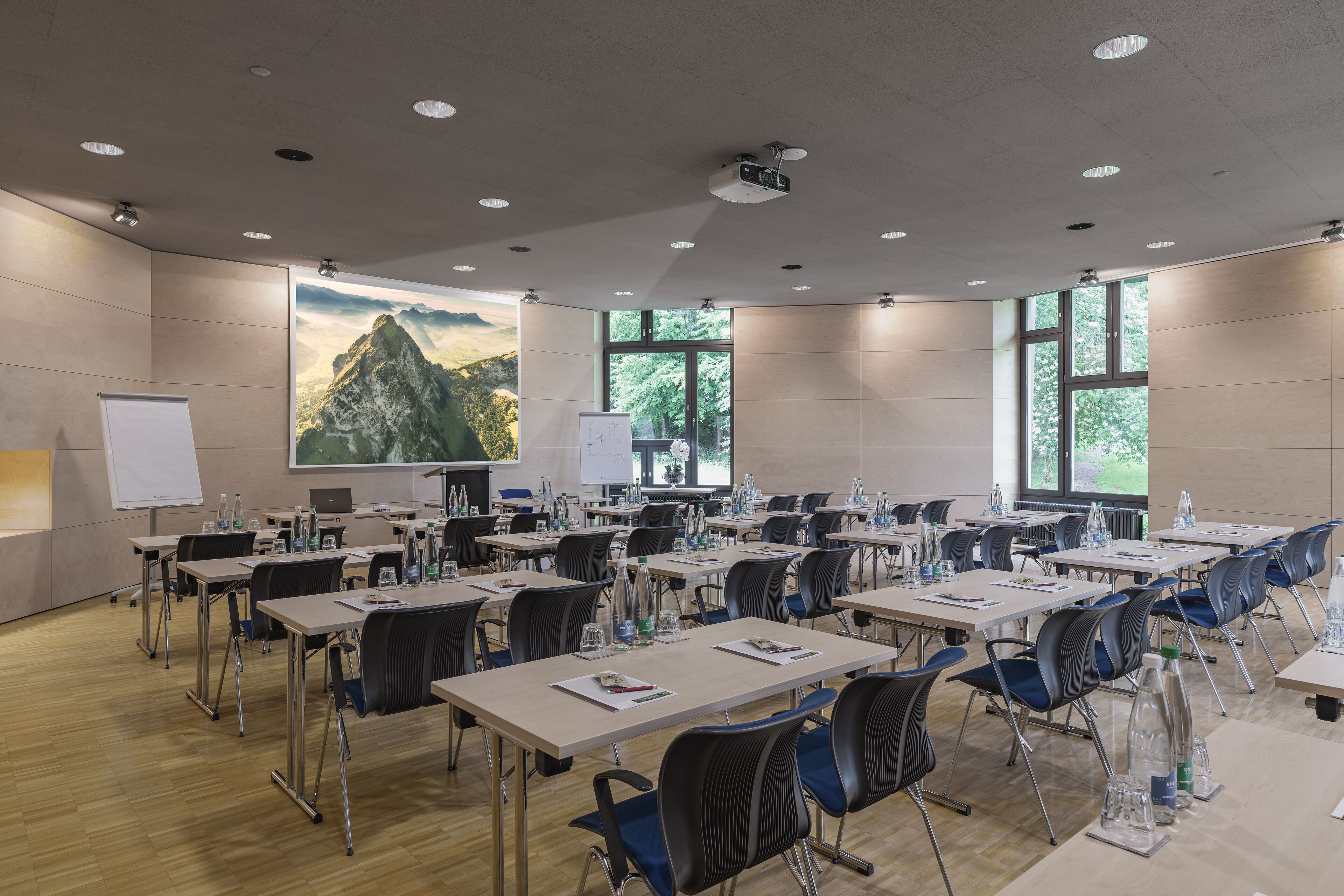 Una sala de conferencias con varias mesas, sillas, una pizarra y una pantalla de proyector.