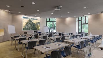 Una sala de conferencias con varias mesas, sillas, una pizarra y una pantalla de proyector.