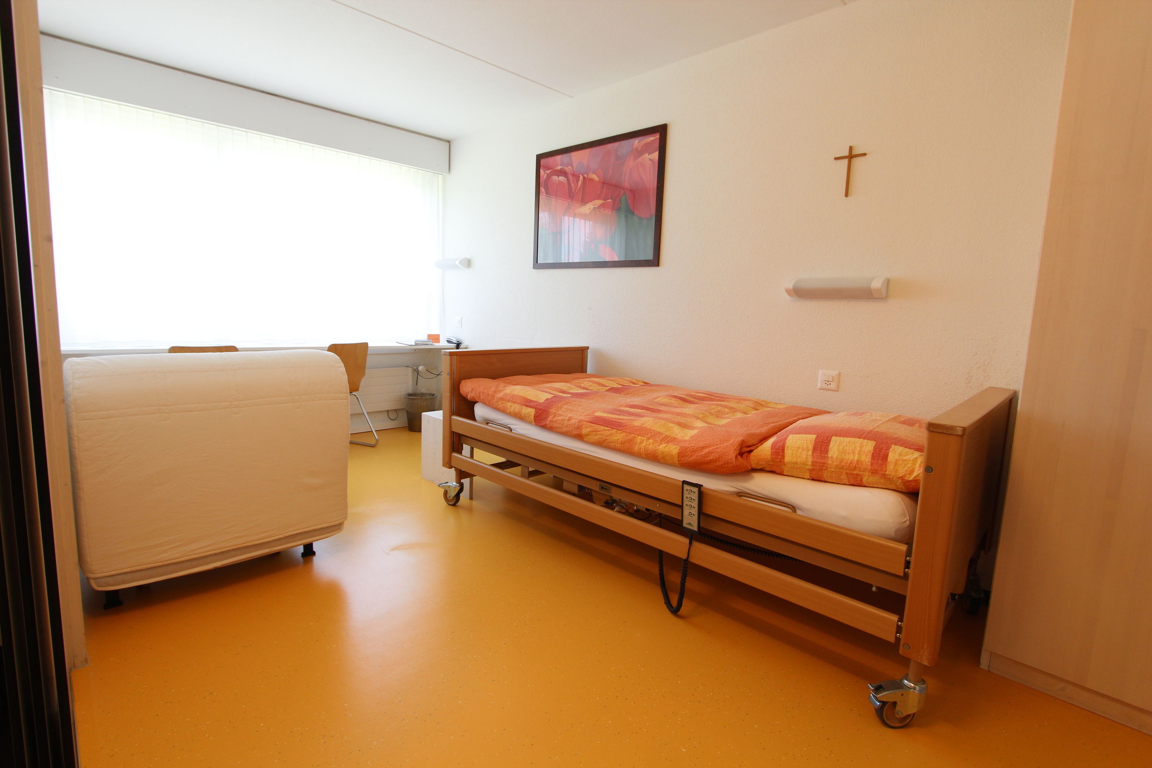 Una habitació d'hospital amb un llit individual, un escriptori i una cadira.