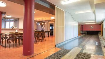 Un hall d’hôtel moderne avec un long couloir, des tables et des chaises en bois, et un pilier rouge.