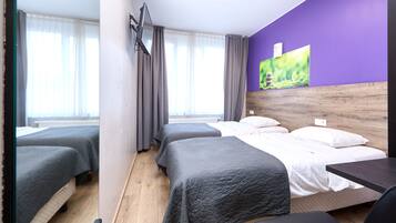 A hotel room with two beds, a wooden headboard, a desk, and a window with curtains.