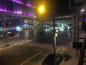 Ein beleuchtetes Stadtbild bei Nacht, mit einem modernen Gebäude, das violette Beleuchtung, eine Fußgängerampel und ein Schild für die Innenstadt zeigt.