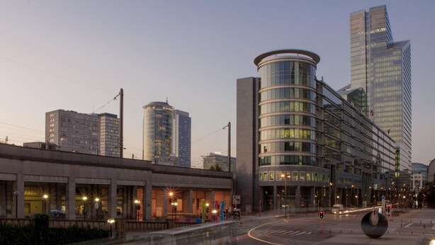 Una intersección urbana moderna con edificios contemporáneos, una rotonda y farolas.