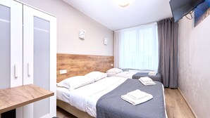 Habitación de hotel con dos camas, cabecera de madera, televisor de pantalla plana y ventana con cortinas.