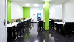 Un comedor moderno con sillas negras y mesas blancas, paredes de acento verde y un suelo negro pulido.