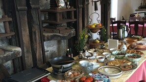 A buffet table with various food items and utensils, set against a rustic backdrop with wooden beams and a stone wall. - Agriturismo Case Tabarani (Collesano)