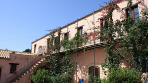 A building with a pink facade, a staircase leading to a balcony, and potted plants. - Agriturismo Case Tabarani (Collesano)