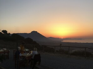 A table set outdoors with a view of a sunset over a body of water and mountains.