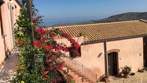 A building with a tiled roof, a staircase, and a view of the sea. - Agriturismo Case Tabarani (Collesano)