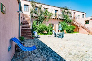 A courtyard with stone flooring, a blue lounge chair, a table with chairs, and a staircase leading to an upper floor.