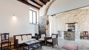 A cozy living room with a stone wall, a wooden ceiling, and a bar area with bottles. - Agriturismo Case Tabarani (Collesano)