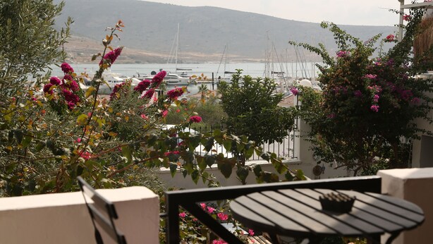Ein Balkon mit Tisch und Stühlen mit Blick auf eine Marina, in der Boote liegen, vor einer Bergkulisse.