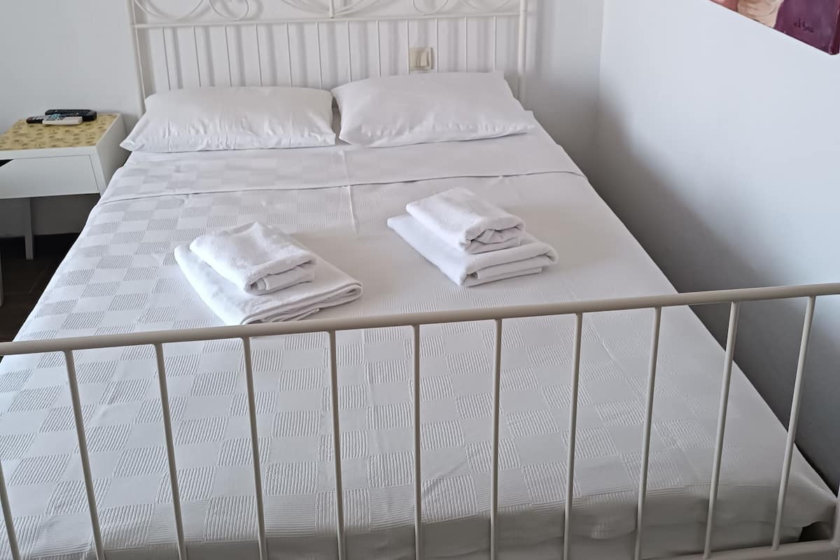 Una cama de metal blanco con un cabecero decorativo, almohadas blancas y toallas dobladas sobre la cama.
