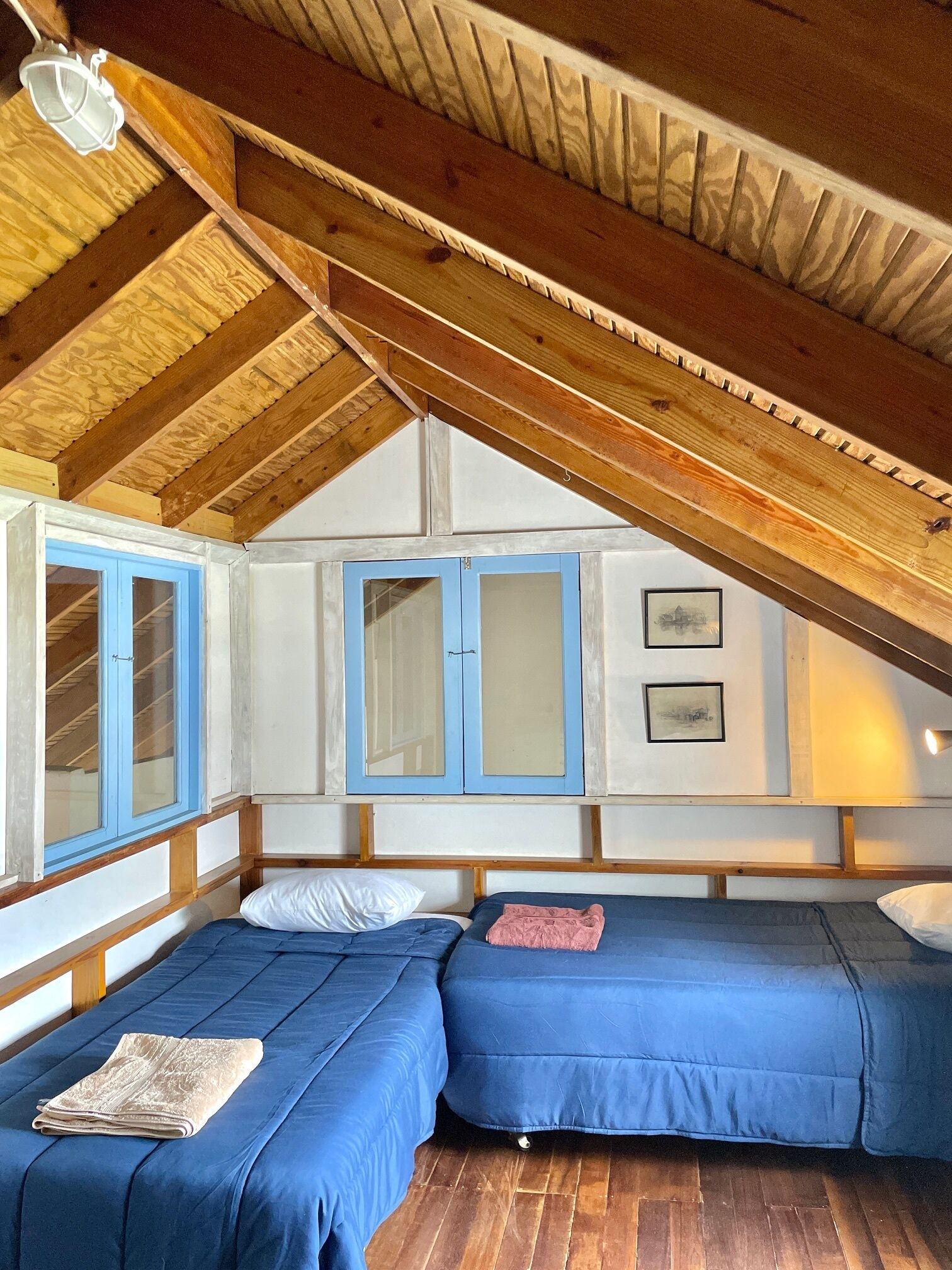 A cozy attic bedroom with two beds, wooden beams, and a sloped ceiling.