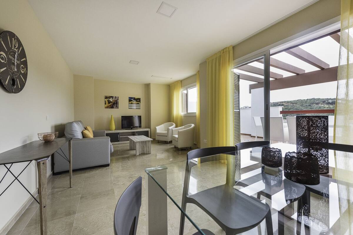 Un salon moderne comprenant un canapé, un téléviseur et un coin repas avec des chaises et une table.