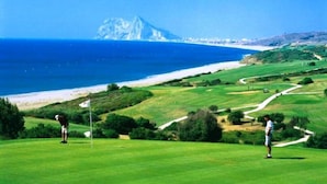 En golfbane med udsigt til havet og et bjerg i det fjerne.