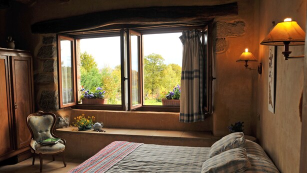 Ein gemütliches Schlafzimmer mit einem Bett, einem fensterbelaubten Fenster, einem Sessel und einer Lampe.