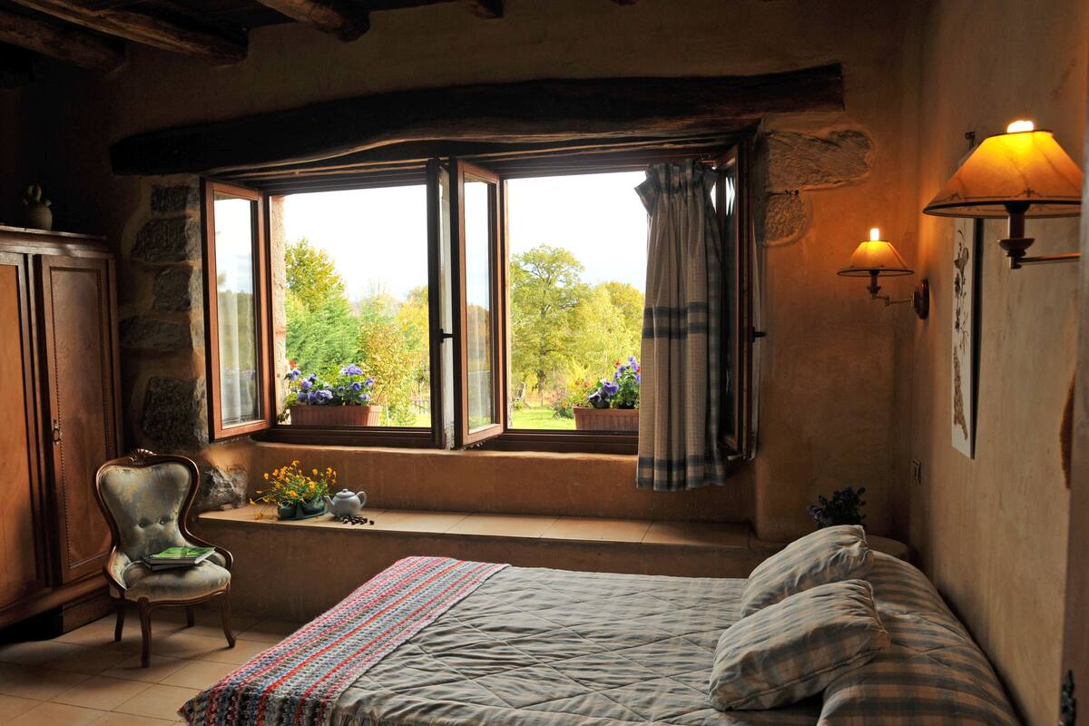Une chambre confortable avec un lit, une fenêtre avec des rideaux, une chaise et une lampe.