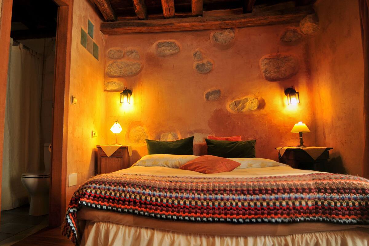 Une chambre confortable avec un lit, deux lampes de chevet et un mur décoré de pierres.