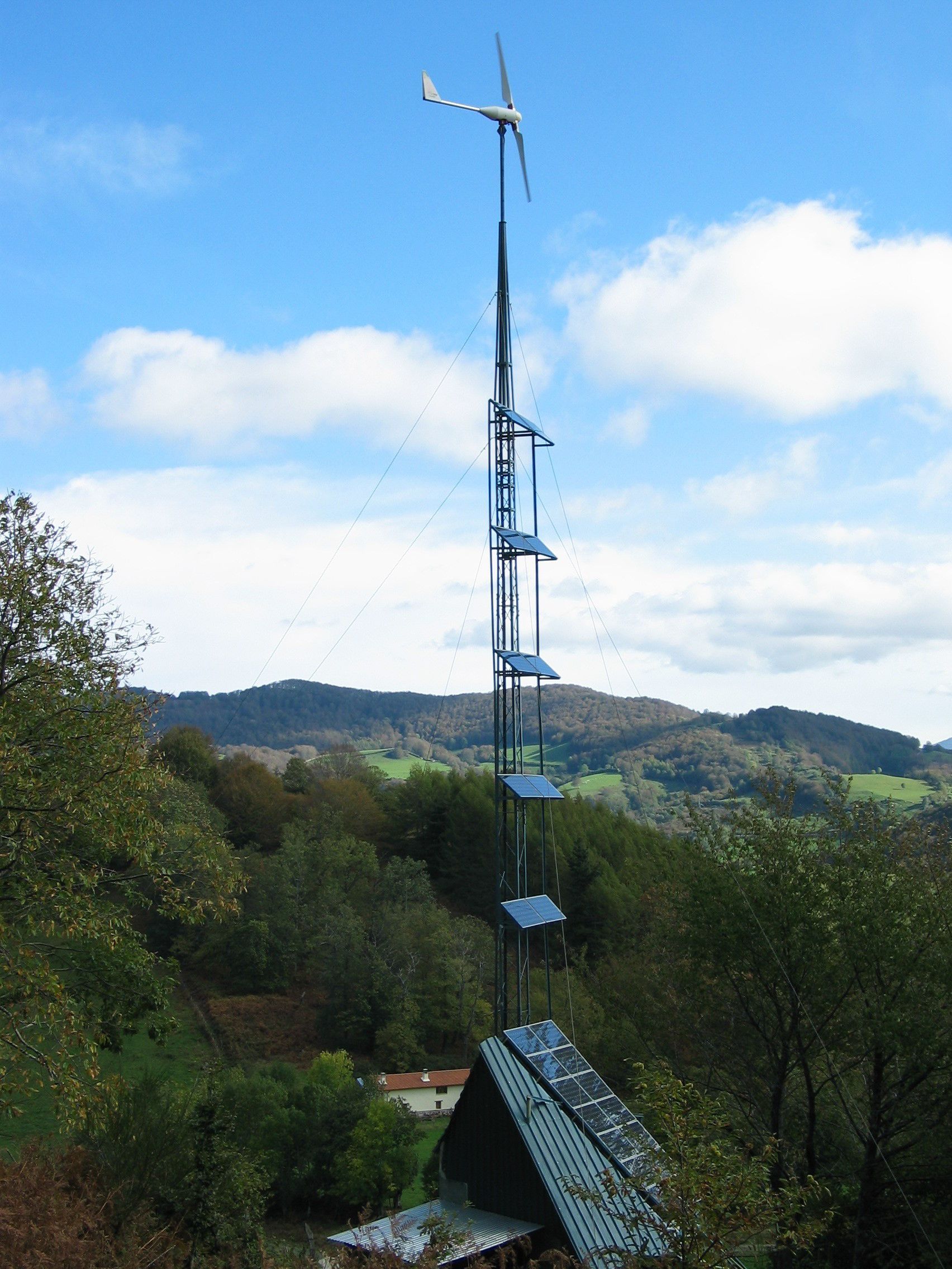 Eine Windturbine mit Solarpanels auf einem Metallturm in einer hügeligen Landschaft.