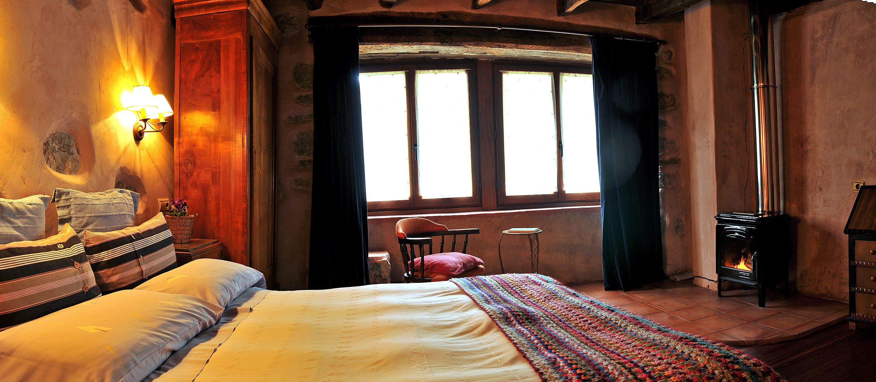 Une pièce confortable avec un lit, une chaise, une petite table et une cheminée.