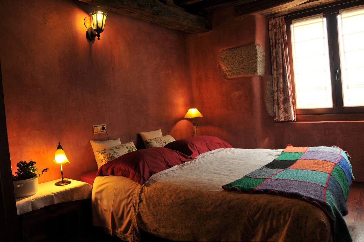 Une chambre confortable avec un lit en bois, deux lampes de chevet, une fenêtre avec des rideaux et un fauteuil.