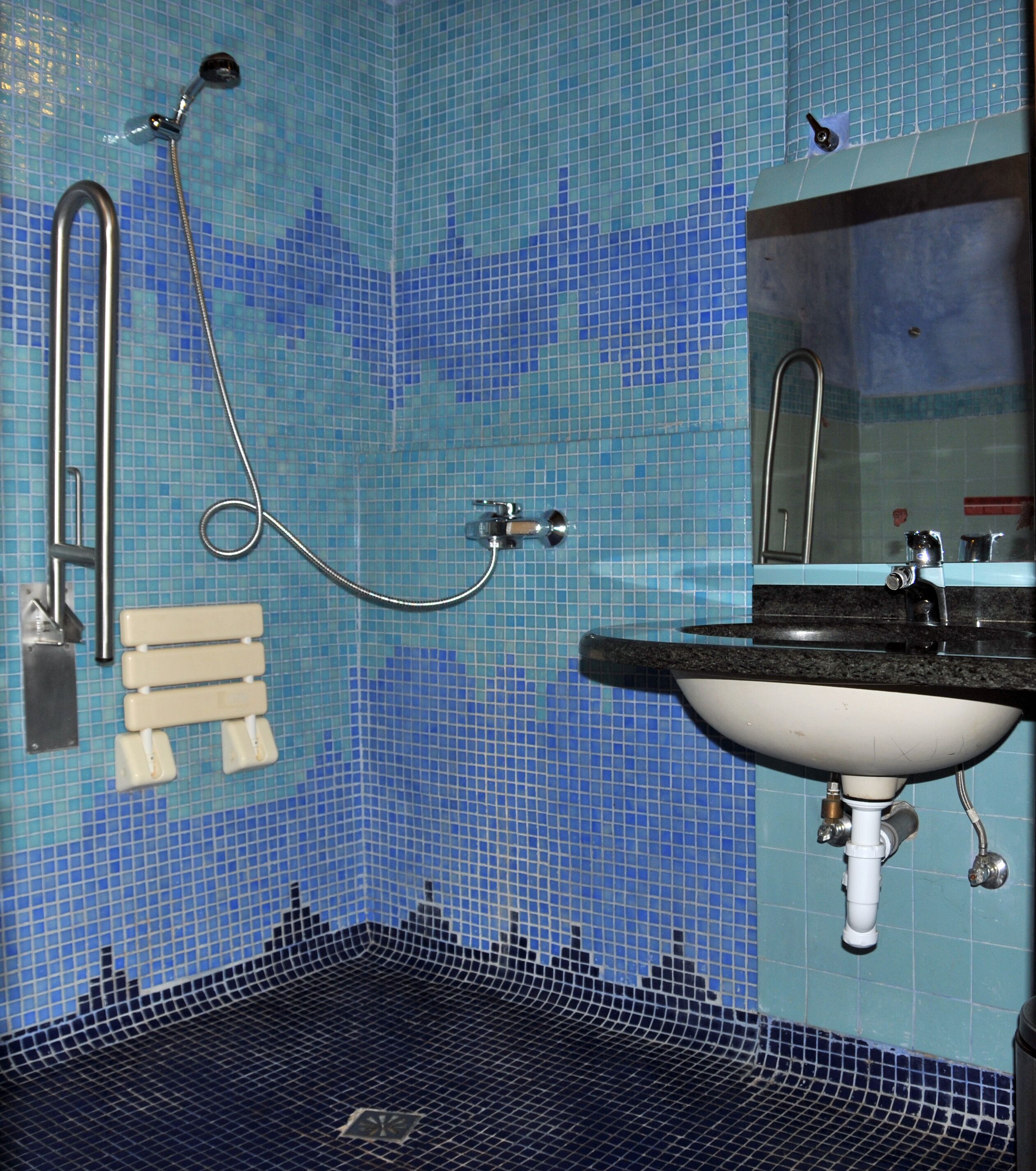 A bathroom with a blue mosaic tile wall, a black sink, a mirror, and a shower with a handheld showerhead.
