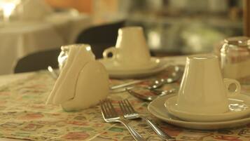 Una mesa servida con tazas, platillos y cubiertos sobre un mantel estampado.