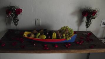 Una mesa con un tazón lleno de fruta colorida y un florero con rosas rojas a cada lado.