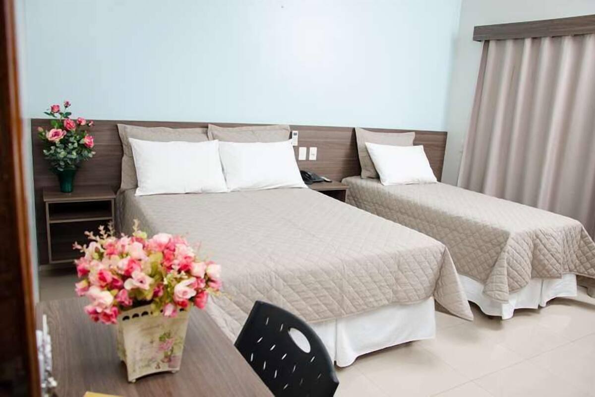 A hotel room with two beds, a desk, and a chair. There are floral arrangements on the desk and a nightstand with a phone.