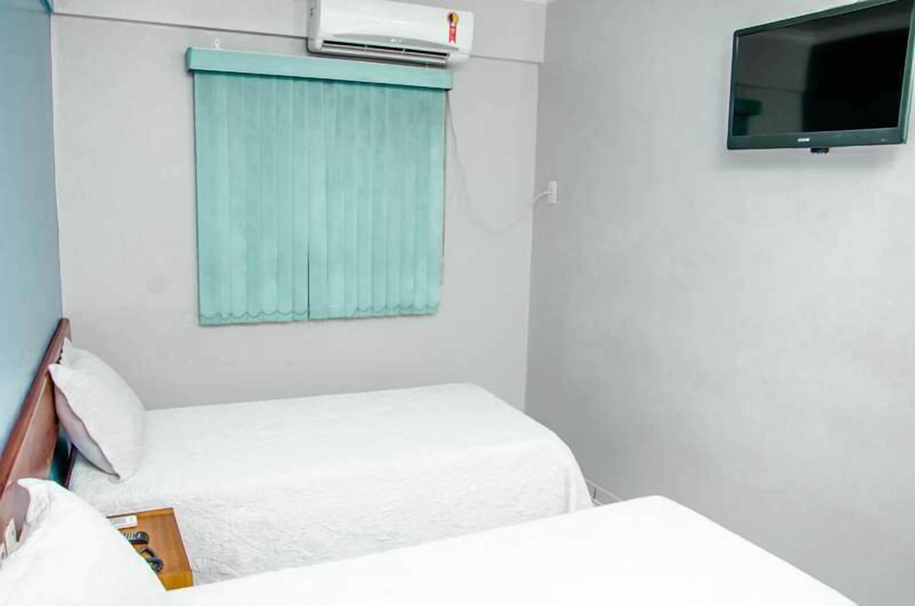 A hotel room with a bed, a TV mounted on the wall, and an air conditioning unit above the bed.