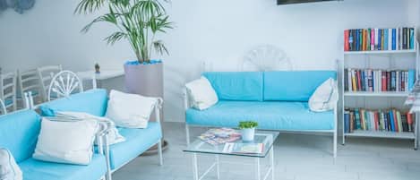 A modern living room with a blue sofa, a white armchair, a glass coffee table, a bookshelf, and a large potted plant.