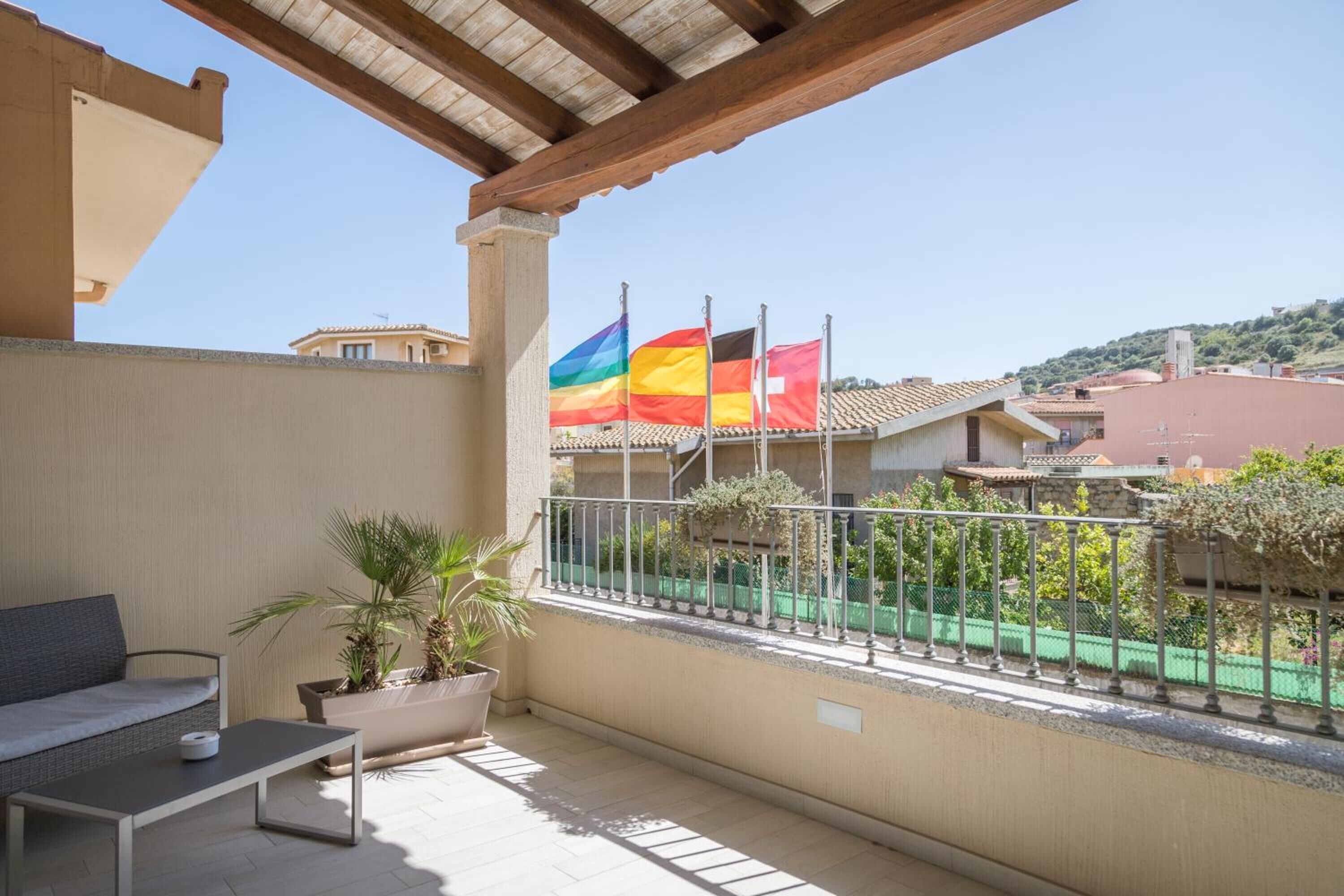 A balcony with a sofa, a small table, and a potted plant. There are two flags on the railing.