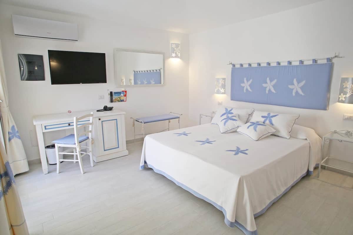 A bedroom with a bed, a desk, a chair, a TV, and a bathroom.