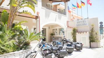 Entrada de un hotel con un letrero que dice 'HOTEL REGINA', un espacio al aire libre cubierto con plantas y varias motocicletas estacionadas al frente.