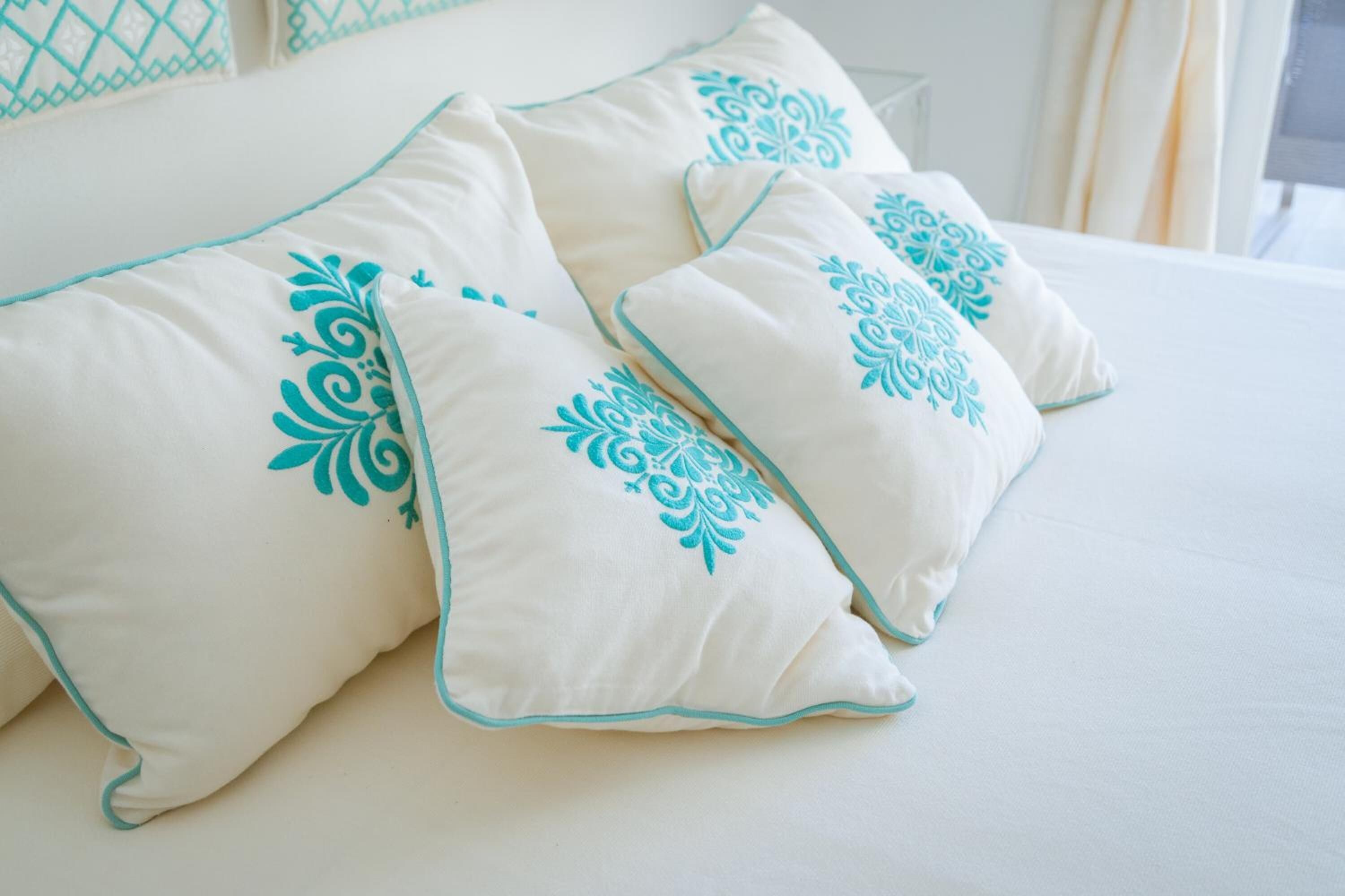 A bed with white bedding and teal decorative pillows.