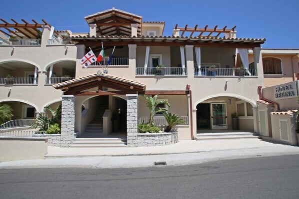 Un hôtel de style méditerranéen, doté d’une entrée centrale avec un porche abrité, de nombreux balcons et d’une enseigne indiquant qu’il s’agit d’un hôtel.