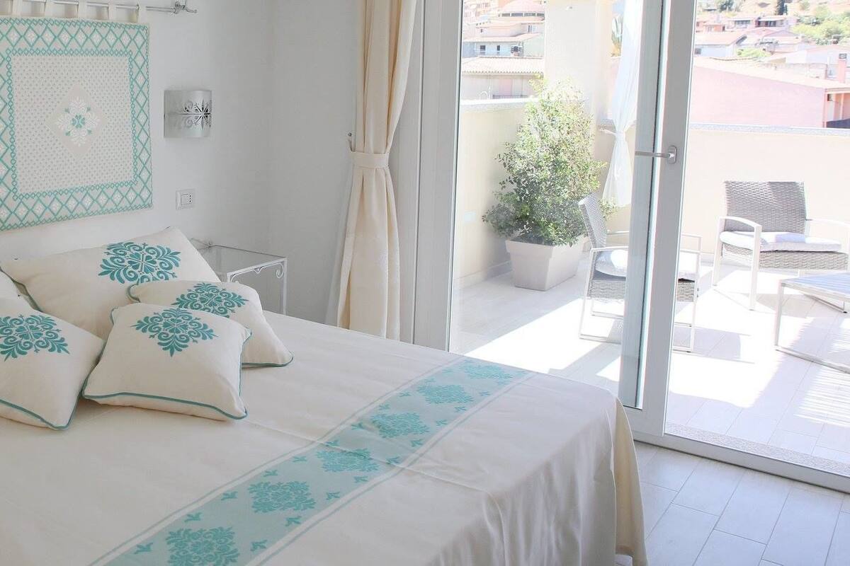A bedroom with a bed, pillows, a nightstand, a potted plant, and a view of the outside balcony.