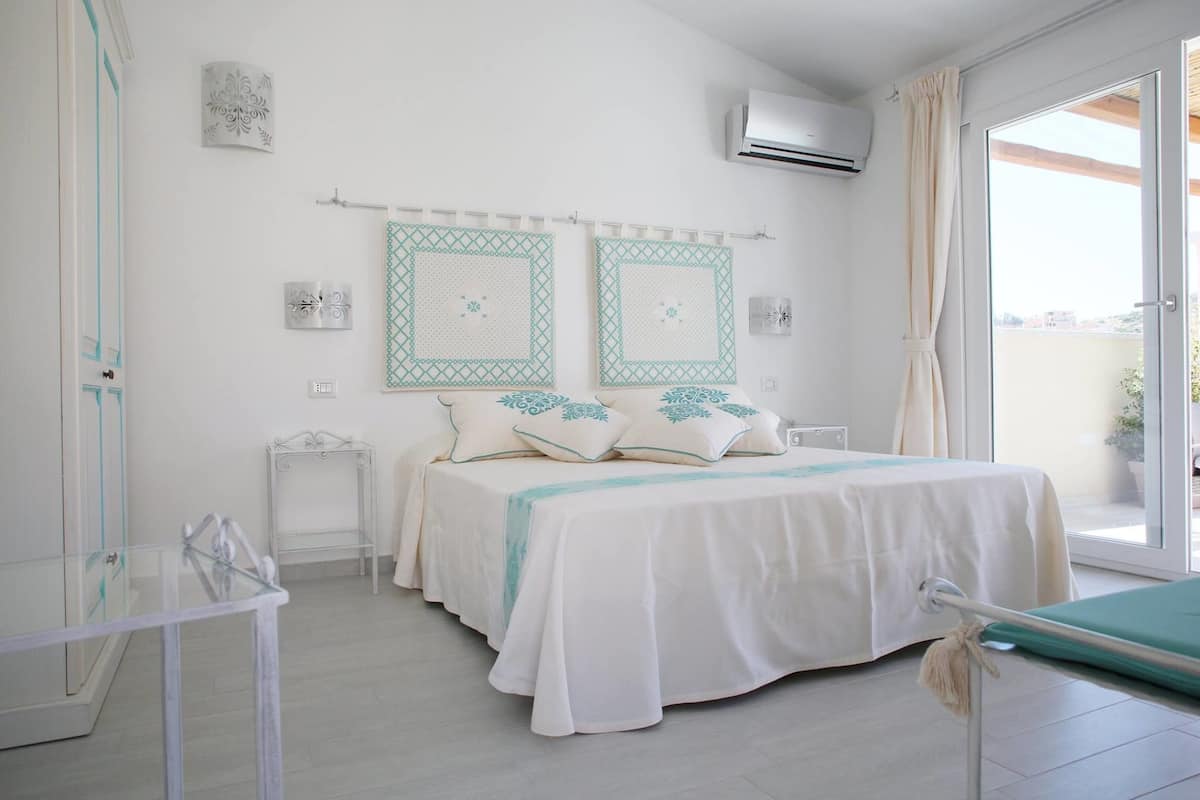 A bedroom with a bed, bedside tables, a glass table, and a view of the outside.