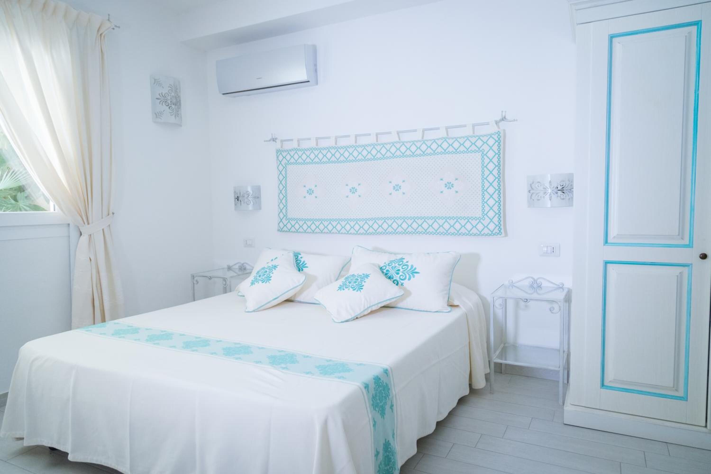 Un dormitorio con cama, mesita de noche, aire acondicionado instalado en la pared y puerta con detalles azules.