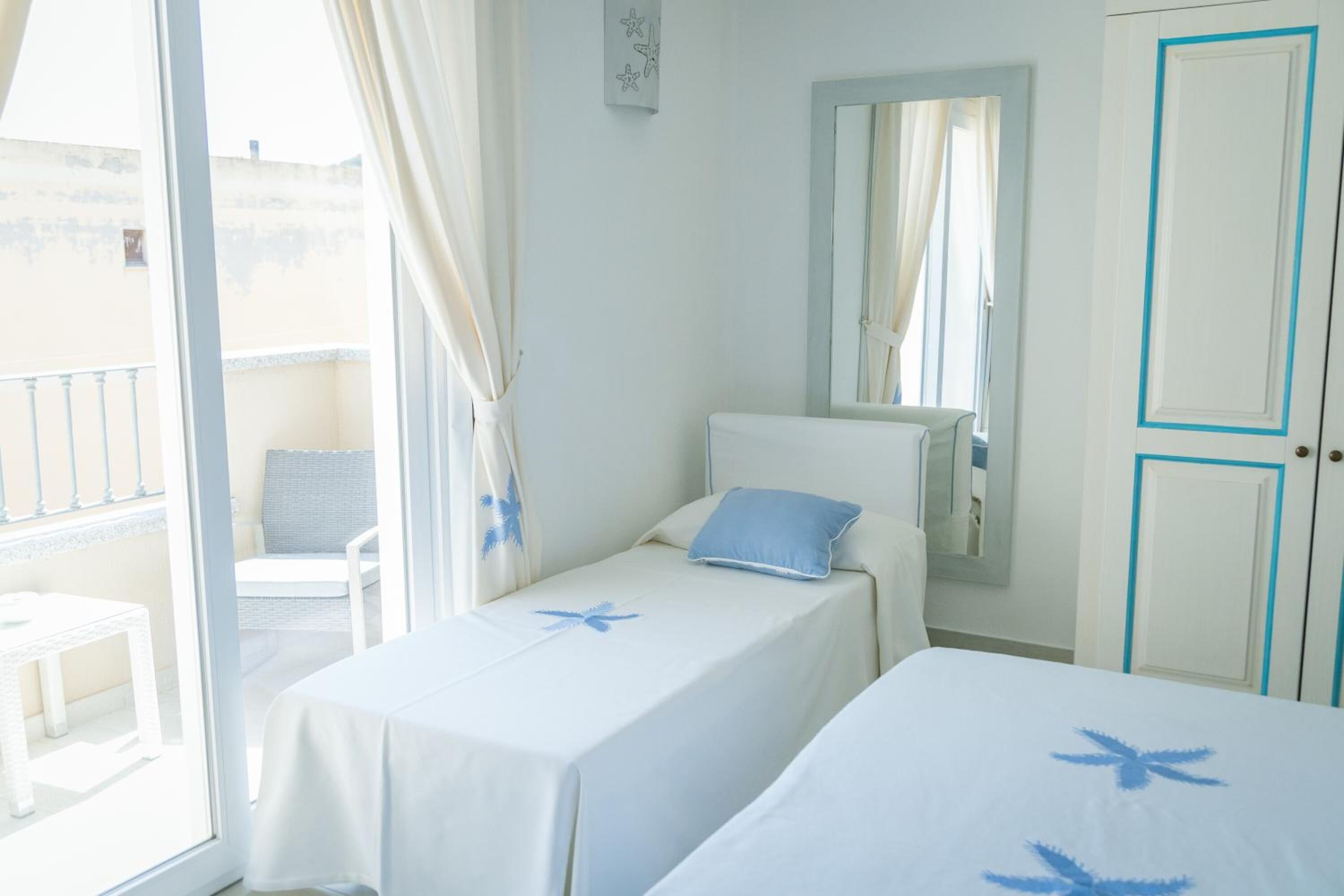 A hotel room with two single beds, a balcony with a chair, and a view of the outside.