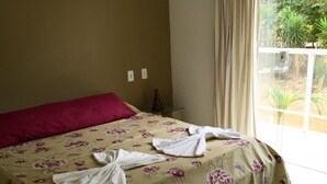 Habitación de hotel con una cama cubierta con ropa de cama floral, una almohada roja y dos toallas blancas dobladas sobre la cama.