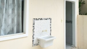 Un baño con un lavamanos blanco, una ventana con cortina estampada y una pared con azulejos.