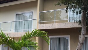 Un edificio de dos pisos con balcón, un árbol pequeño y un jardín con acolchado rojo.