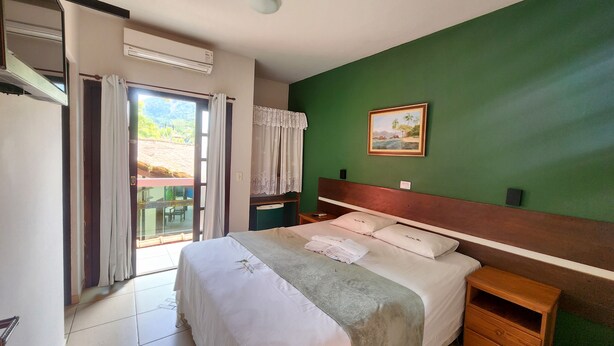 A bedroom with a bed, a nightstand, a green wall, and a painting. - Pousada Parcel das Ilhas (São Sebastião)