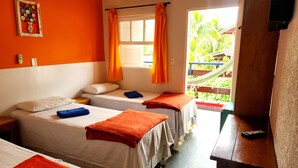A room with two beds, each with a white mattress and orange towels. There is a window with orange curtains, a hammock outside, and a remote control on a wooden table. - Pousada Parcel das Ilhas (São Sebastião)