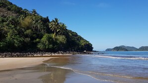 A beach with a rocky shoreline, palm trees, and a clear blue sky. - Pousada Parcel das Ilhas (São Sebastião)